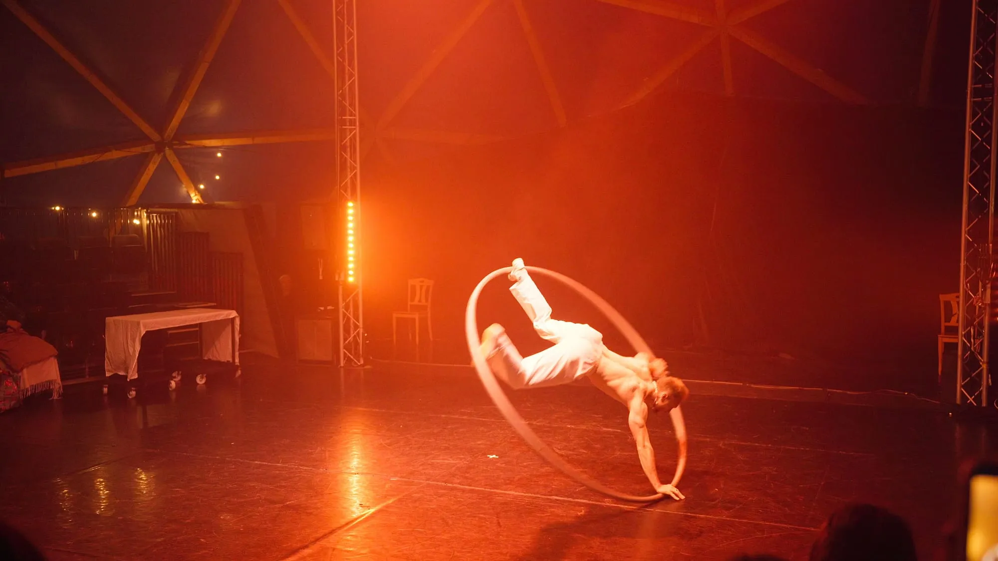 Das Cyr Wheel kippt zur Seite, die Beine in der Luft, auf der Bühne im roten Licht