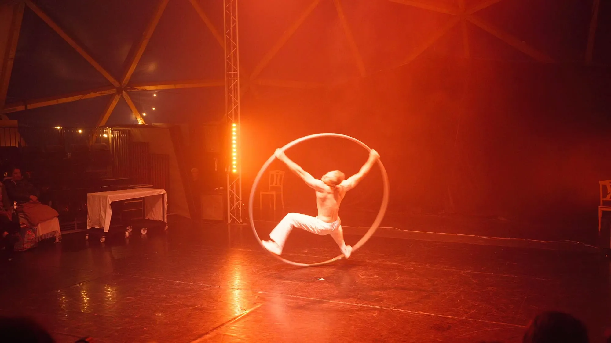 Arme und Beine zum Stern gespreizt im Cyr Wheel, auf der Bühne im roten Licht des Pepe Dome