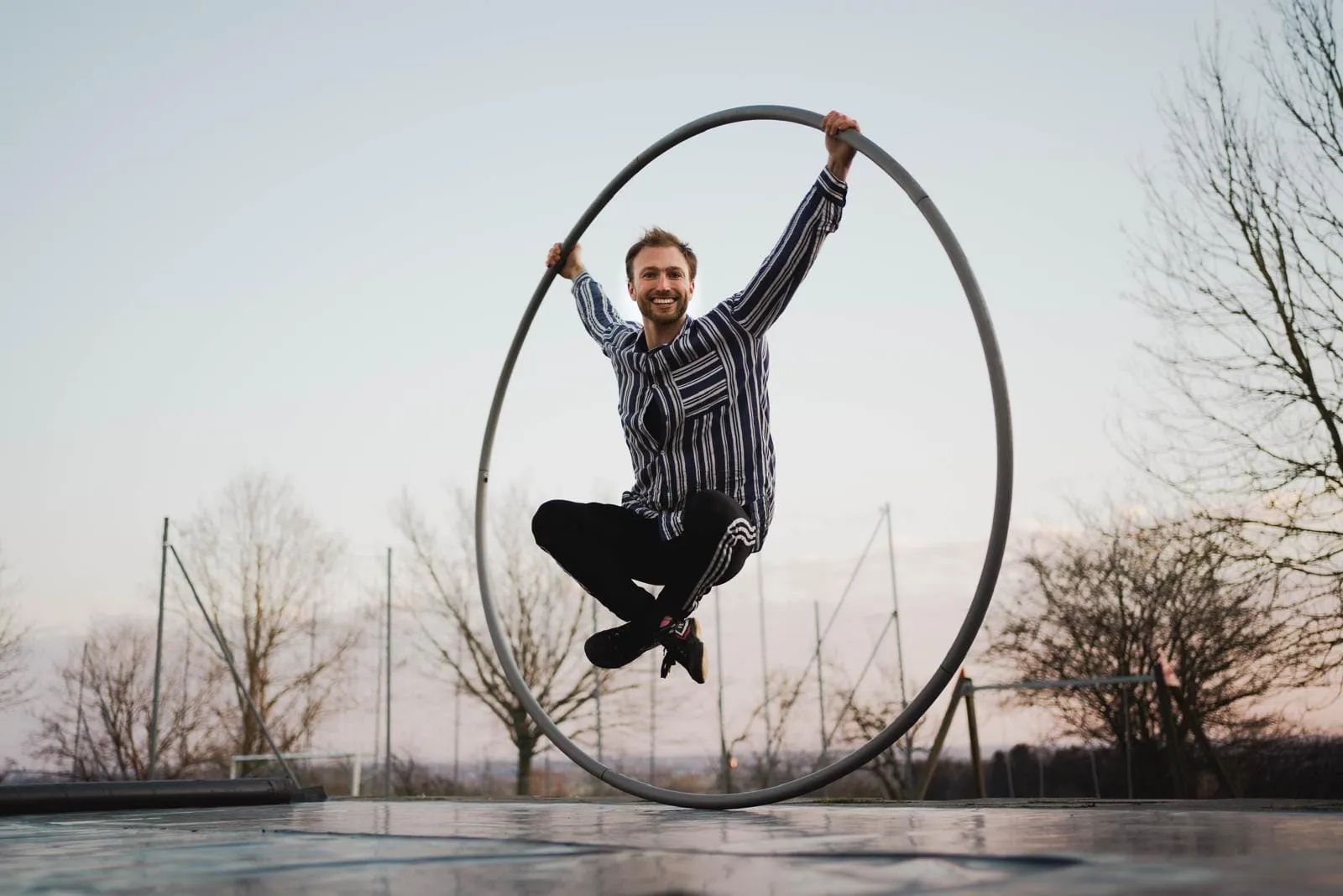 Mit angezogenen Knien im Cyr Wheel, die Hände oben am Reifen, draußen in der Abenddämmerung