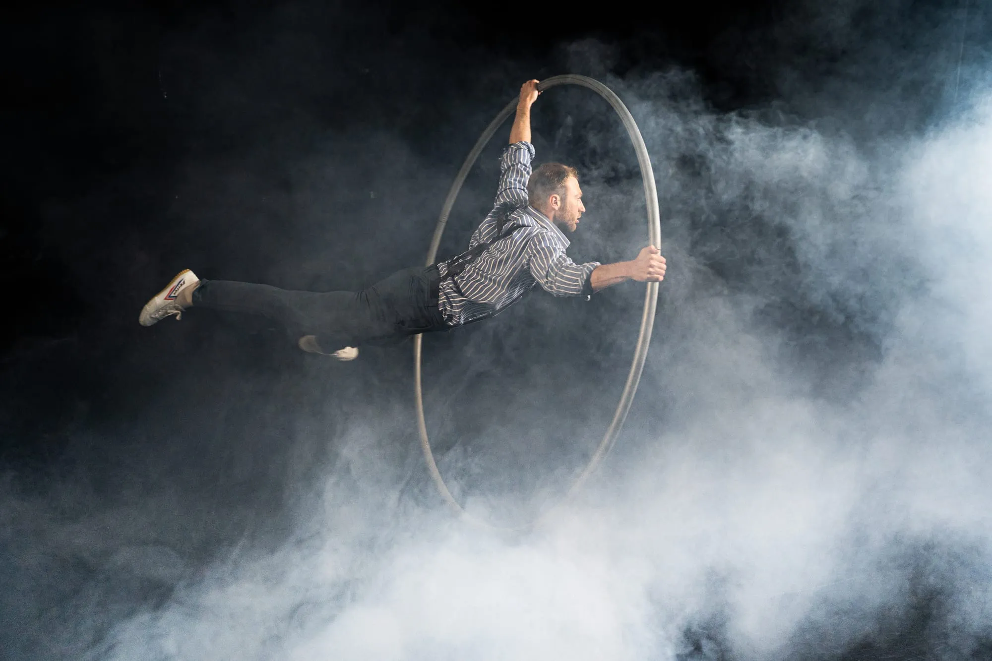Waagerecht in der Luft, mit beiden Händen am Cyr Wheel, umgeben von Bühnennebel